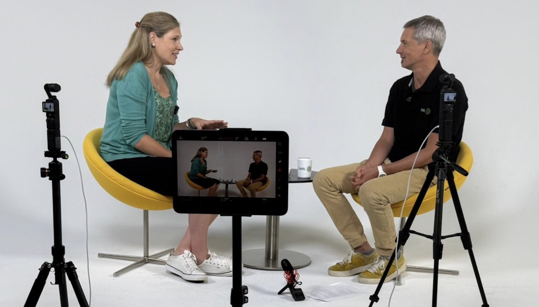 Two people speaking surrounded by recording equipment.