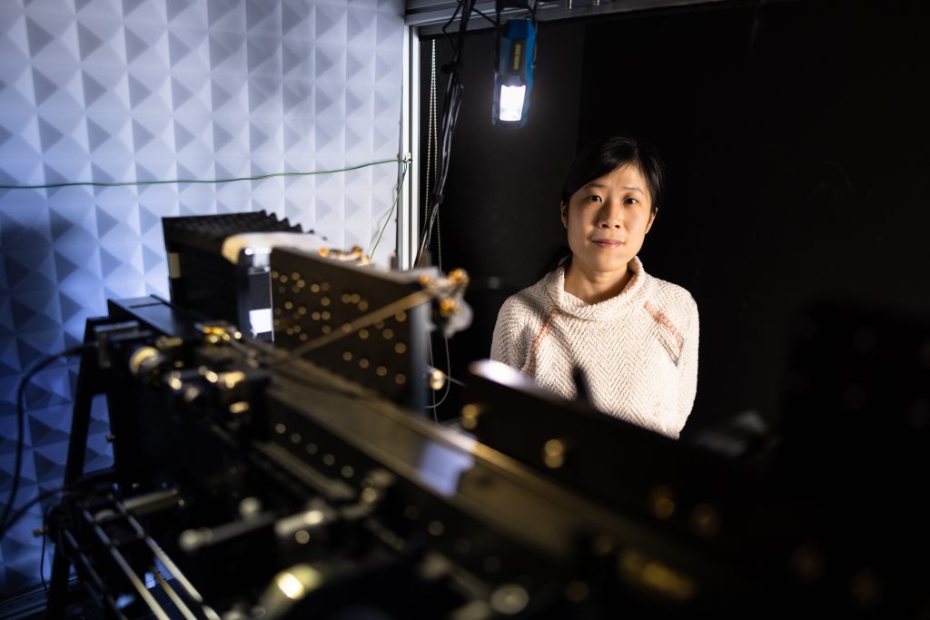 Female scientist stands in dark room with instrumentation