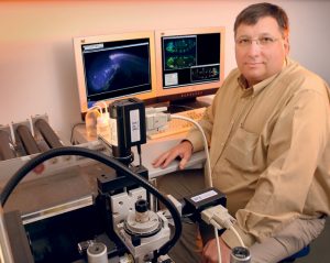 Male scientist sits in front of two computer screens and associated equipment related to SPIM.