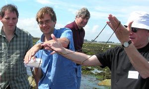 Four scientists look at a worm that appears more like a very long piece of string being held in one scientist’s hands.