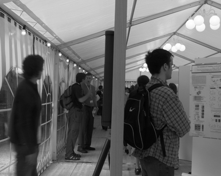 Black and white photo shows participants reviewing posters on displays in large tents