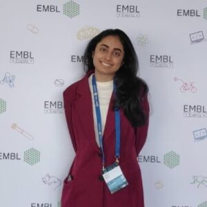 young woman with a conference badge posing in front of EMBL Events photo wall