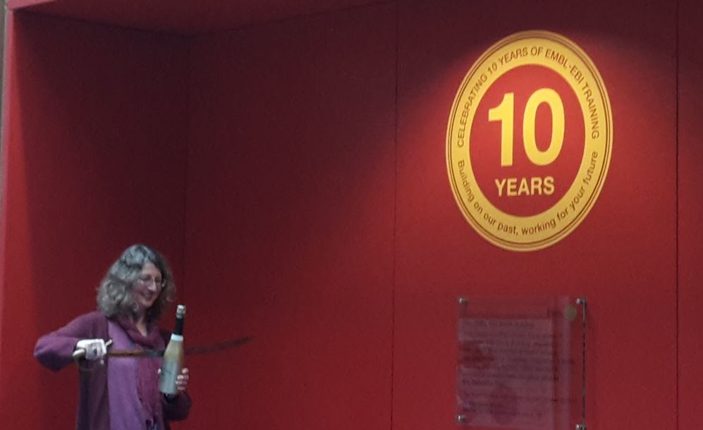 Cath Brooksbank wields a sword to cut the top off a bottle of champagne at an event to celebrate 10 years of the EMBL-EBI Training programme