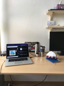 A table with a laptop, a thermos with coffee or tea and a notebook on a desk. 