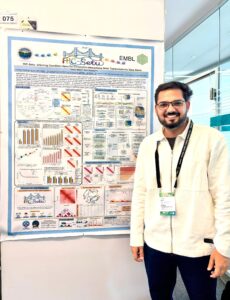 A smiling young man posing in front of a big poster, presenting his research