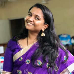 A young woman wearing a purple saree smiling at the camera