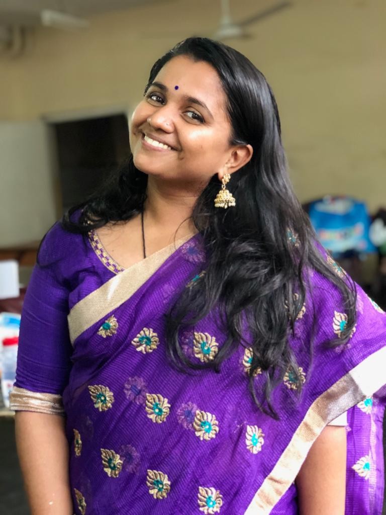 A young woman wearing a purple saree smiling at the camera