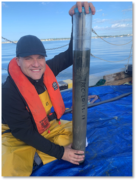 Scientist with a large sample of sediment around one meter in size with ocean in the background