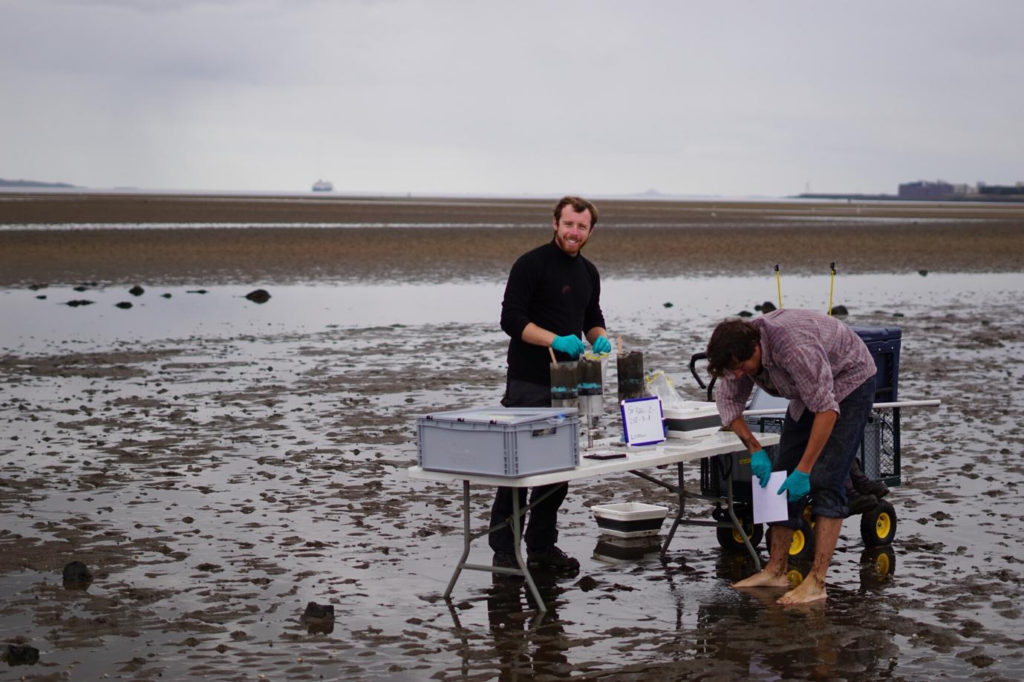 Two scientists on a coastal area of Scotland with a table and apparatus set up to collect surface sediment 