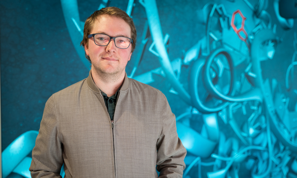 Man standing in front of a wall with scientific imagery including protein structures