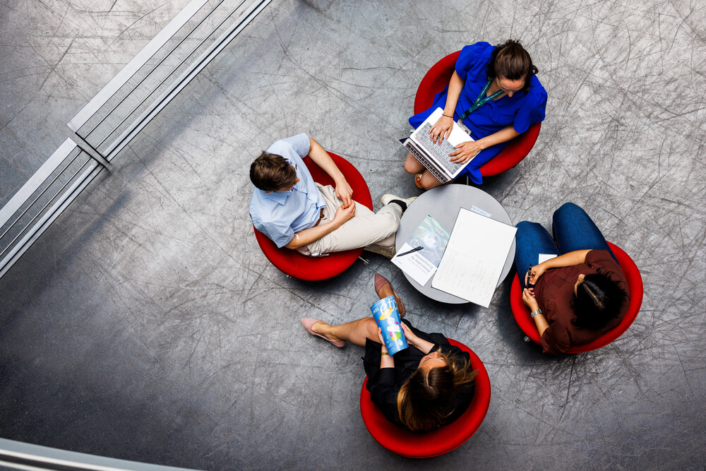 overhead shot showing four people discussing around a desk