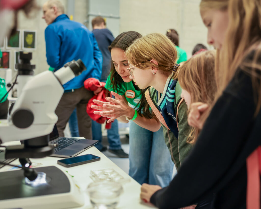 EMBL Mitarbeiterin erklärt einer Besucherin die Funktionsweise eines Mikroskops. 