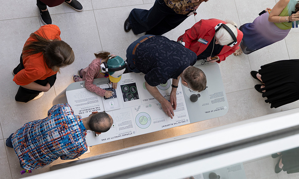Four people interacting with a multisensorial table exhibit by touching its tactile and interactive components and listening to audio descriptions through headphones.