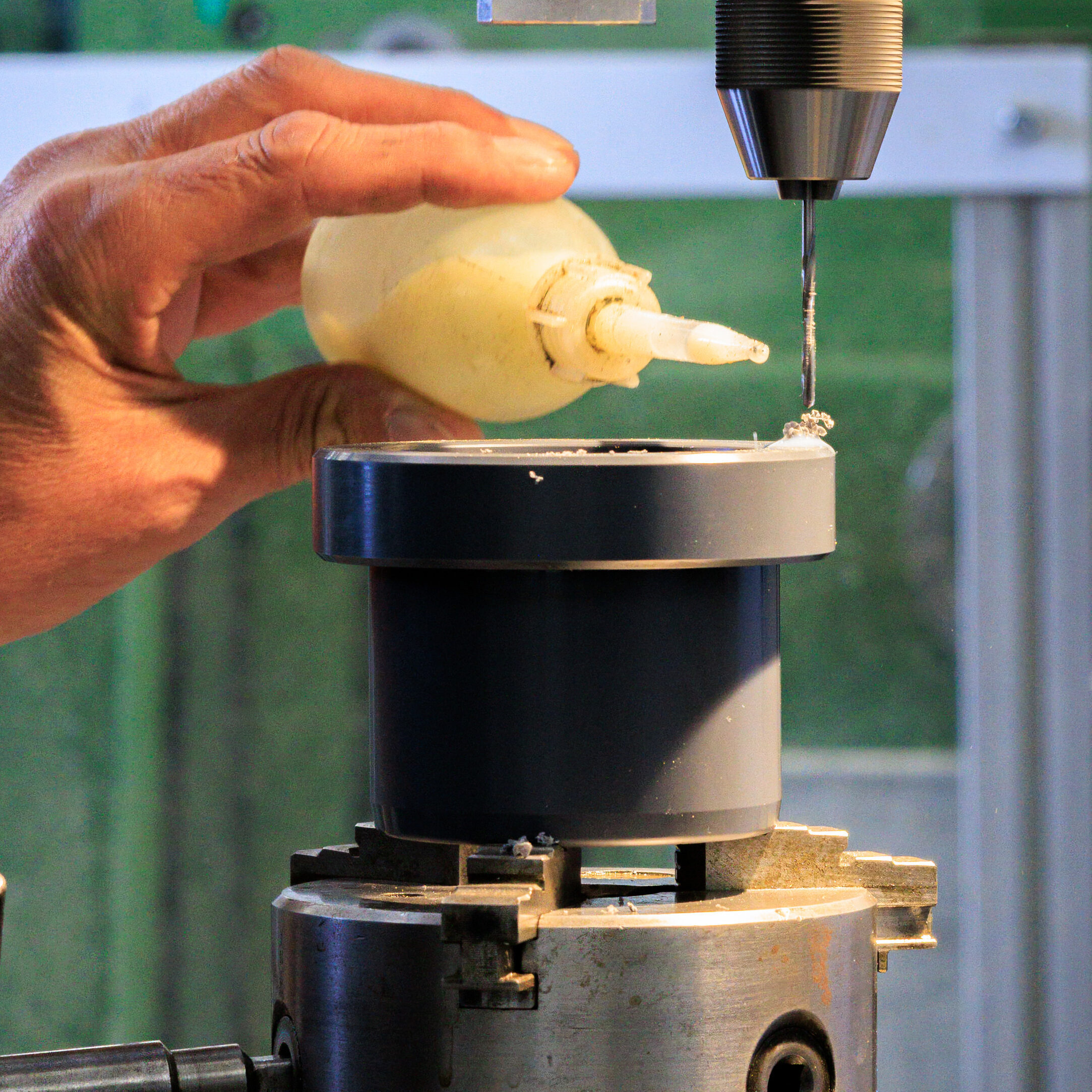 A plastic part mounted in a chuck on a drill press being oiled during machining