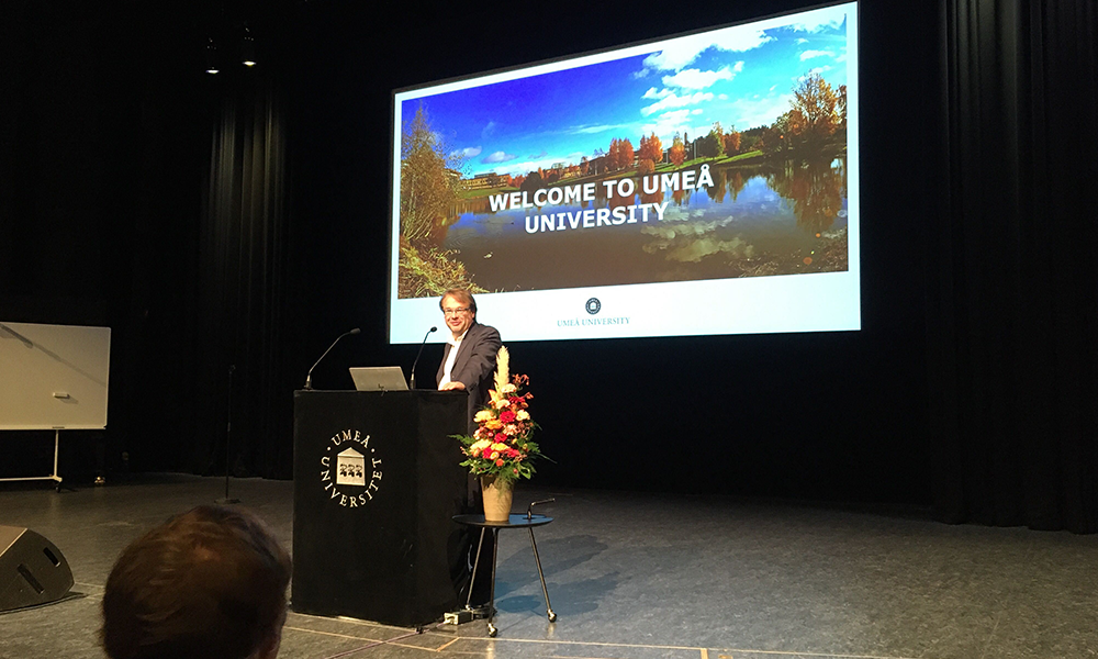 Oliver Billker, Director of MIMS, is standing at the podium in front of a microphone. Behind him, a projected slide says 