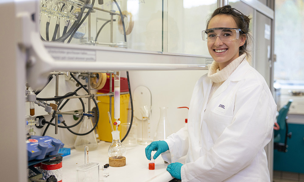 Female scientist in white lab coat stands at chemistry bench in her lab