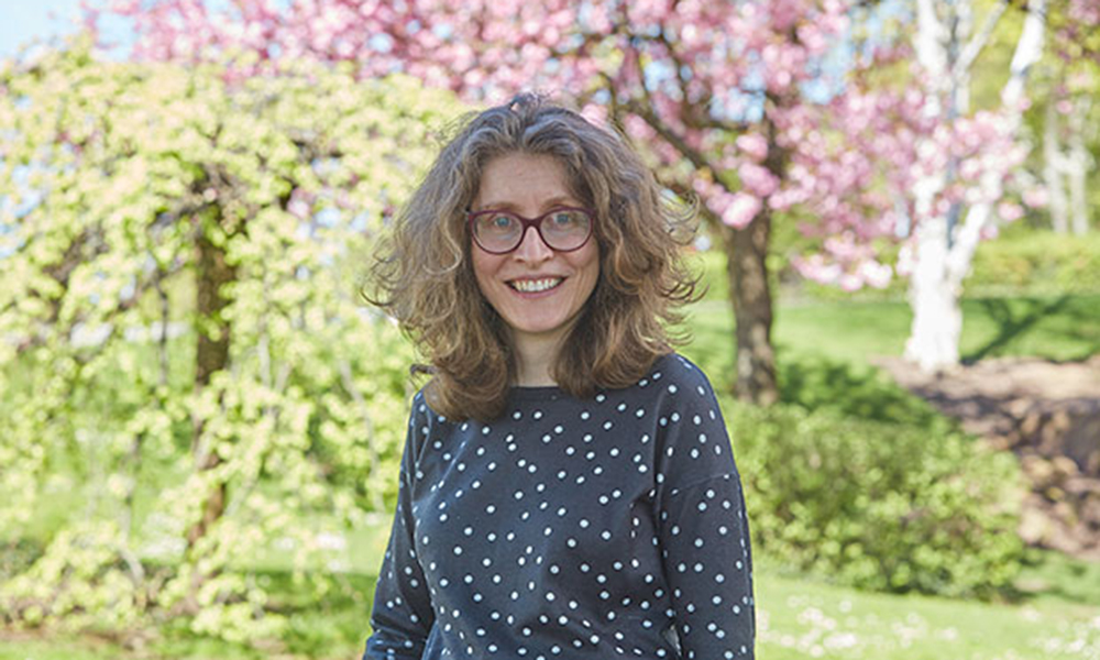 Female researcher stands in front of pink flowering tree