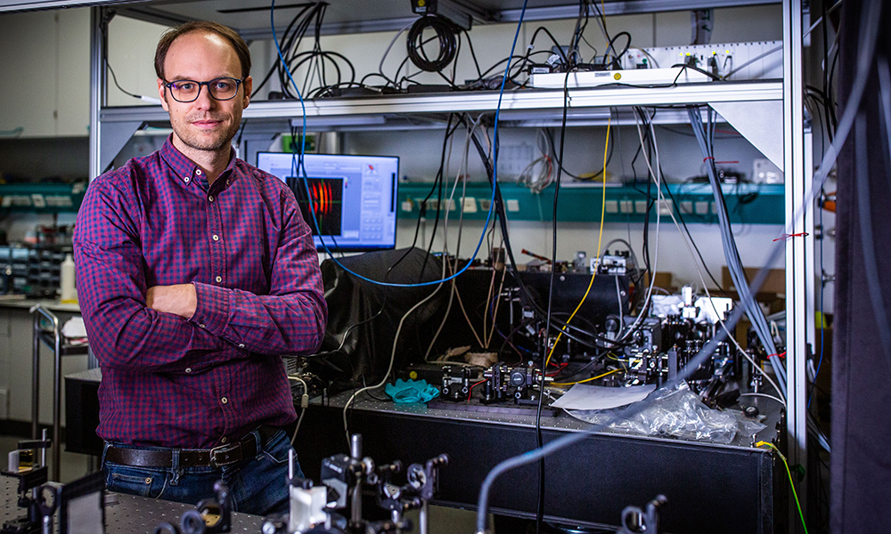 Male scientist stands in front of machinery in his lab.