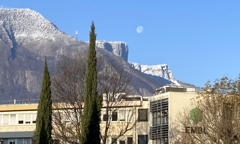 Snowy mountains behind functional buildings. The Moon is up in the sky.