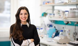 Nicoletta Petridou looks towards the camera smiling, whilst standing in a science laboratory