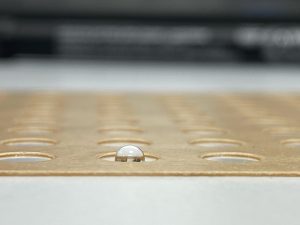 A close-up photo of a shiny droplet of liquid that has been placed into one of the wells of a crystallisation plate.