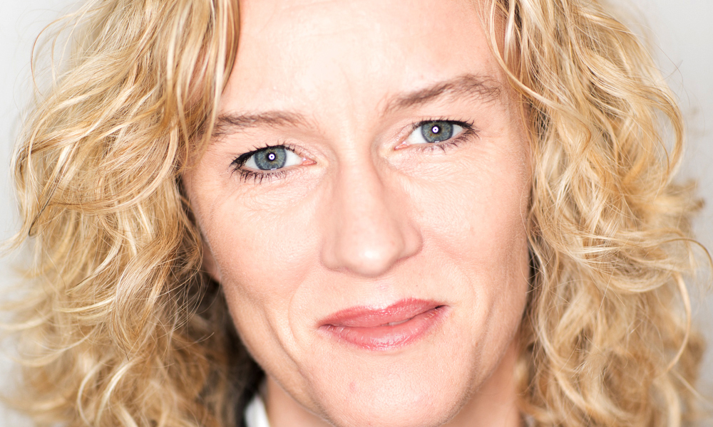 Head shot of female social scientist with blond curly hair and blue/grey eyes.