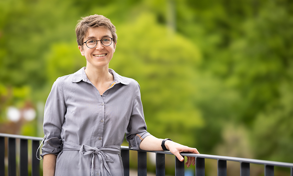 Woman stands at brown railing in front of trees