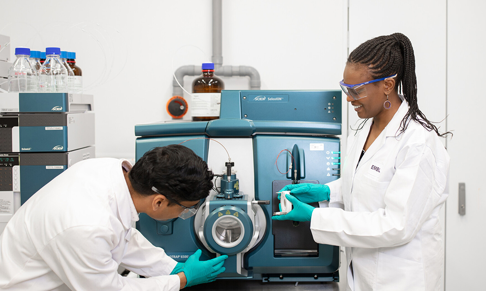 Two scientists in lab coats working on an instrument in the lab.