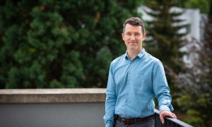 Portrait photo of a man in front of trees on a balcony