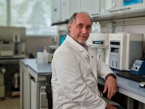 Male scientist in white lab coat sits in front of flow cytometer