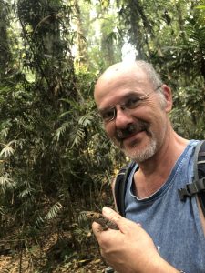 Male scientist stands in jungle holding skink
