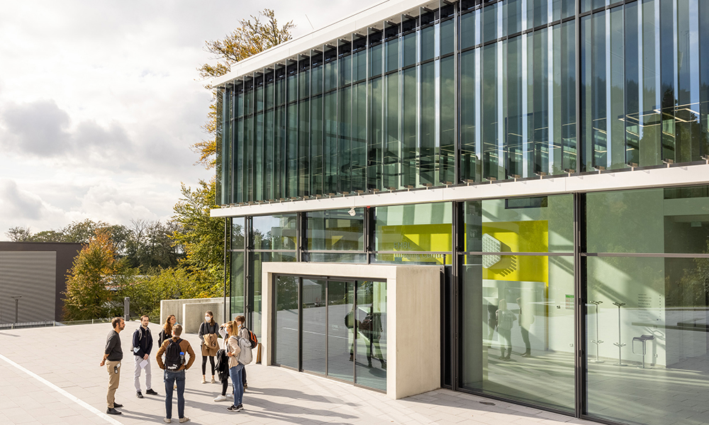 A group of people standing outside a two-storey reseach building, featuring a glass front.