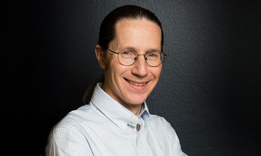 A headshot of Mark Daly with dark background behind him.