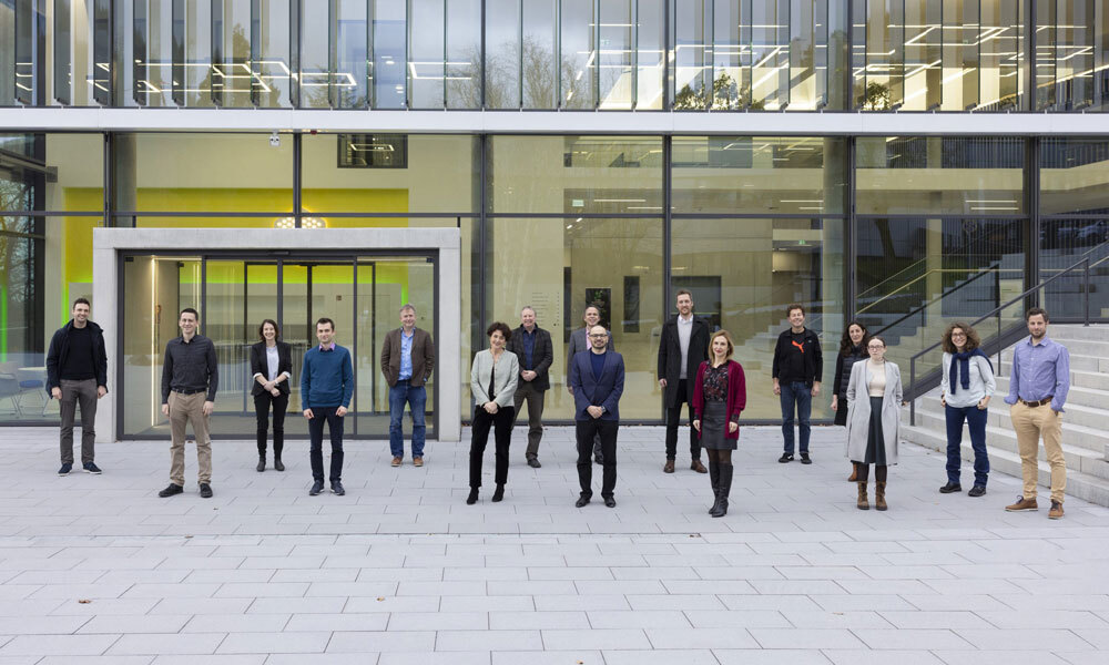 EMBL scientists and DeepMind staff stand together in front of the building of the EMBL Imagine Centre