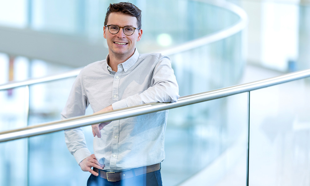 A male scientist in a white shirt stands at a walkway railing.