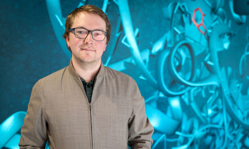 Man standing in front of a wall with scientific imagery including protein structures