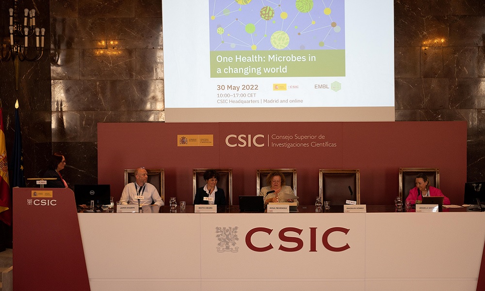 The image shows an auditorium where members of EMBL and CSIC sit at a long table on stage.