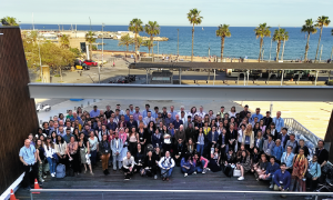 Group of around 100 people posing in a terrace in front of the sea.