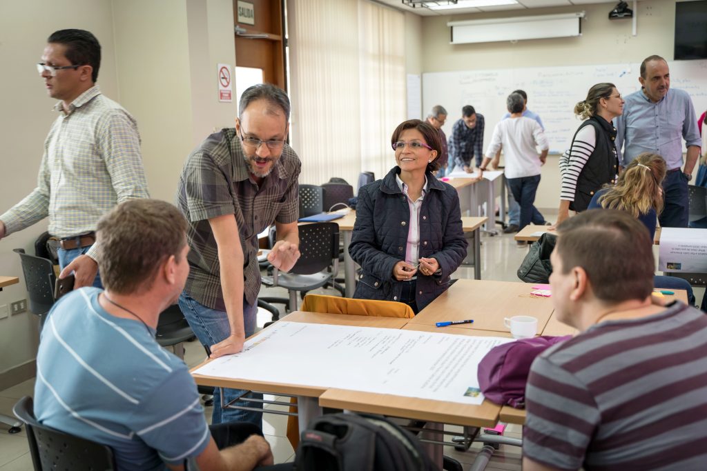 Photograph of four workshop participants seated or standing around a desk. 