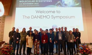 Group photo of speakers and organisers standing in front of a slide saying “Welcome to the DANEMO Symposium”.