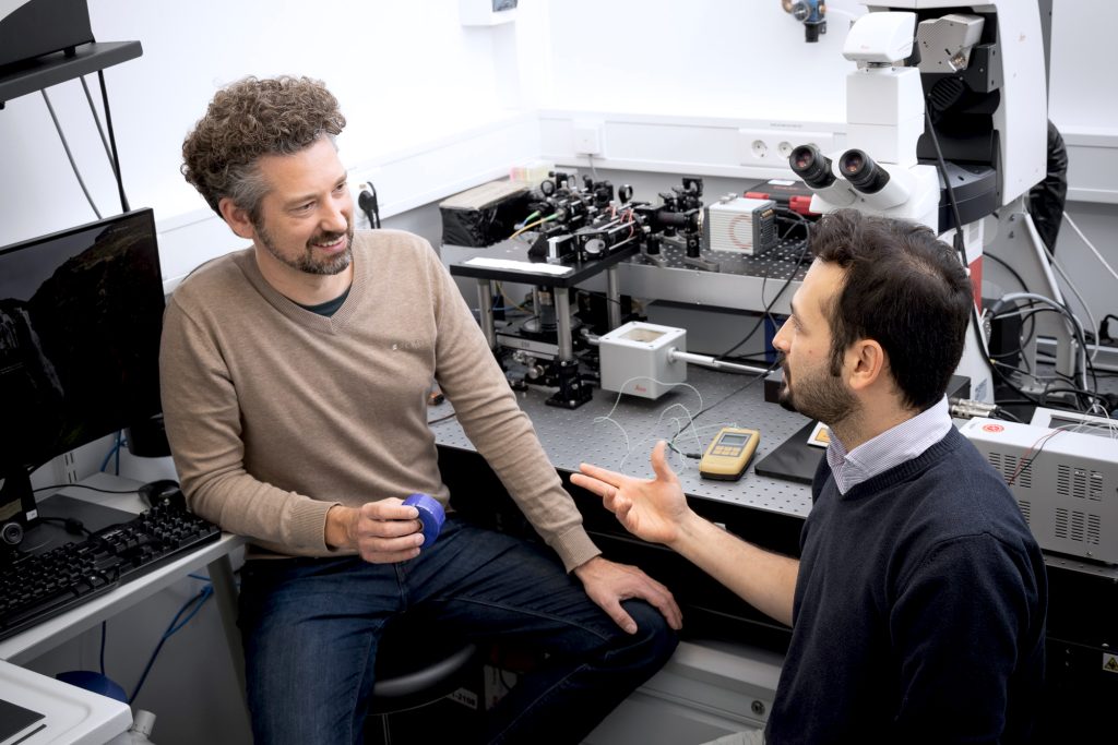Two male scientists in conversation in front of a microscope.