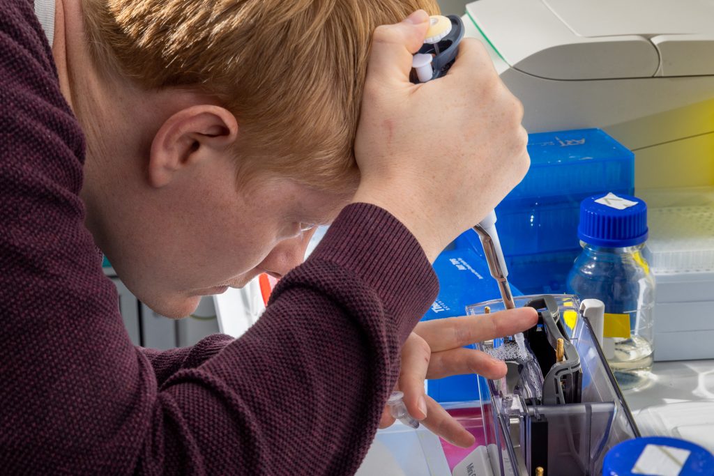 A male scientist holding a pipette and loading a gel. 