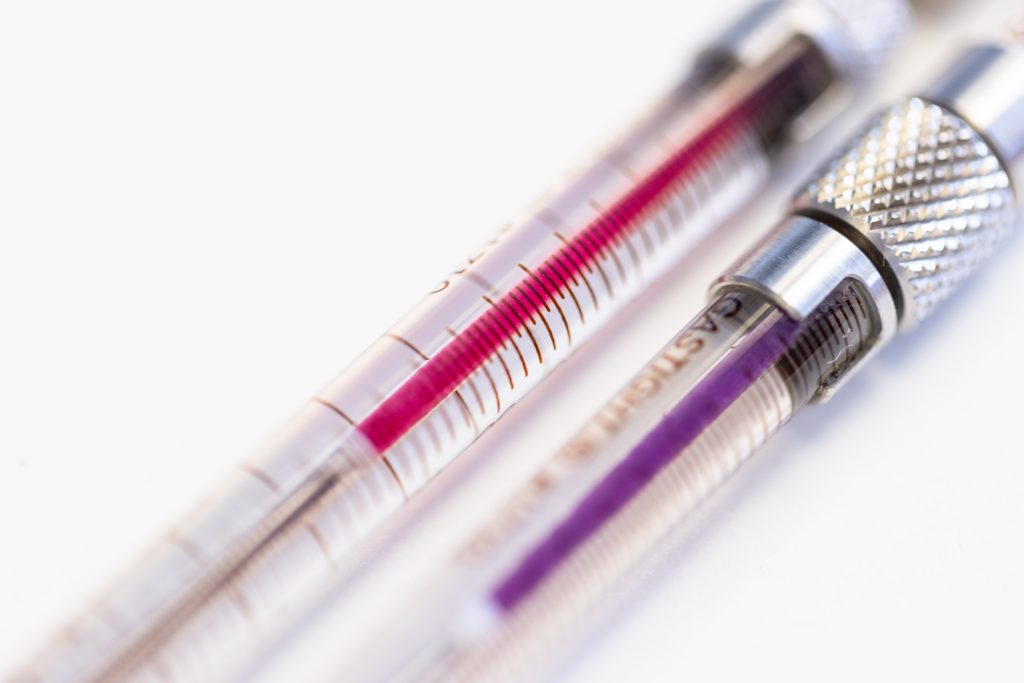Closeup photo of two syringes. One contains purple liquid, the other violet liquid.
