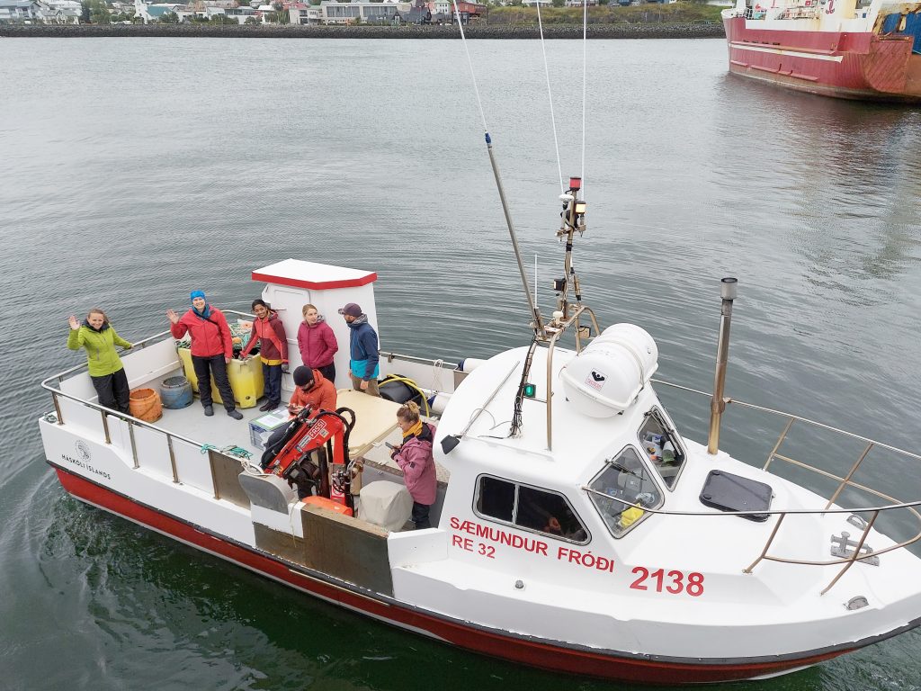 Photograph of a boat with scientists waving from the deck. 