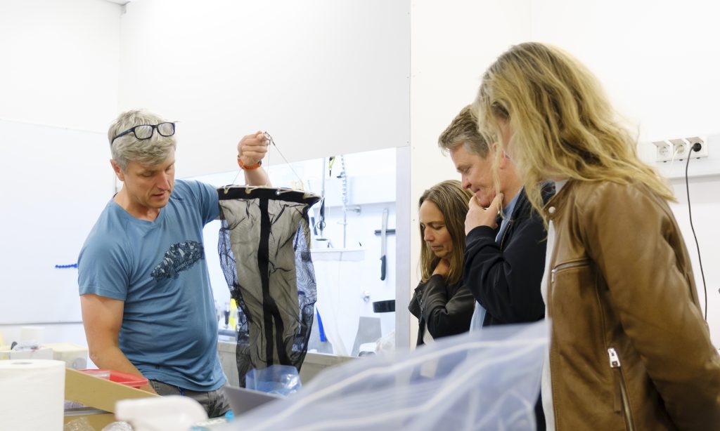 A male scientist holding up a plankton net while other researchers look on. 