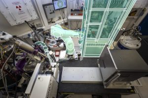 View from above of a small room with several tools, cables and pieces of technology. A rectangular box, a robotic arm and a device are highlighted in green.