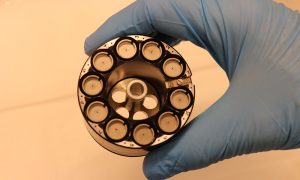 A photo of a hand holding a puck. The puck is a metal cylinder with 10 holes.