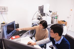 Two scientists sit at desk, consulting information on a computer screen