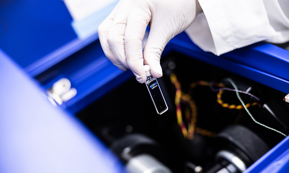 Photo of a human hand introducing a small element into a machine at the SPC Facility.