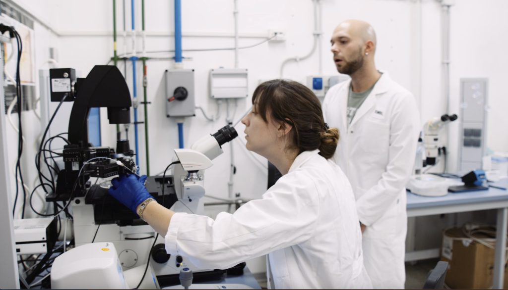 Female scientist in lab coat working on a microinjection setup.